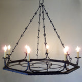 A striking wrought iron chandelier featuring an ornate design, suspended by elegant chains. It holds multiple candle-style lights, enhancing any room's warmth and ambiance.