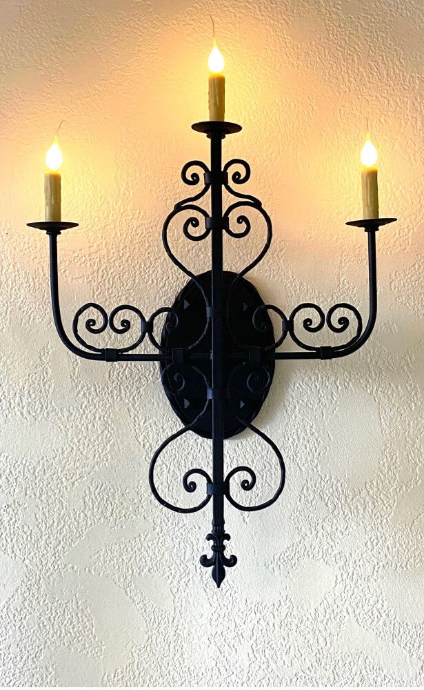 Wrought iron wall sconce featuring elegant scrollwork and three candle-like bulbs. The design adds a rustic charm to any space, enhancing its ambiance.