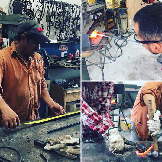 Artisans skillfully work in a workshop, creating custom wrought iron light fixtures. One craftsman measures metal, while others shape glowing hot iron with precision tools. Various completed pieces and equipment are visible in the background, showcasing the craftsmanship involved in making unique wall sconces and hanging fixtures.