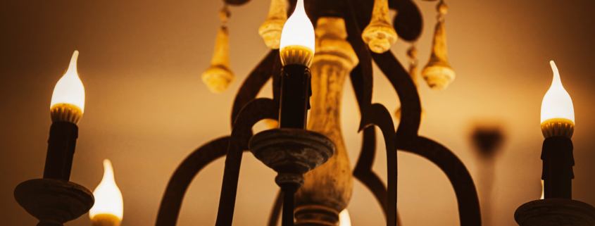 On an old elegant beautiful chandelier, lamps in the form of candles emit a bright cozy light in the evening